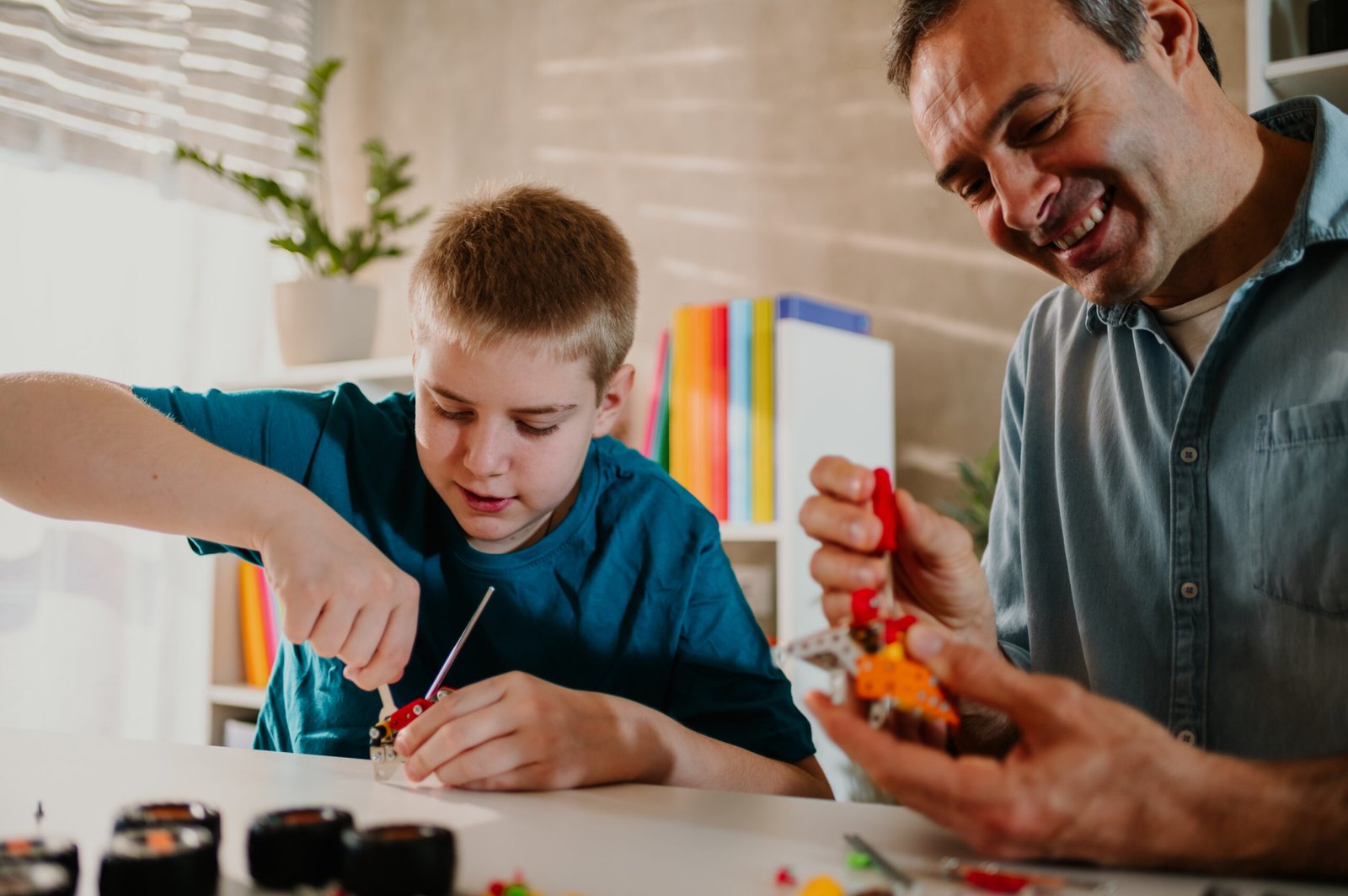 Happy father and his young blond son putting together parts of the toy. A child laughing while playing with wooden blocks