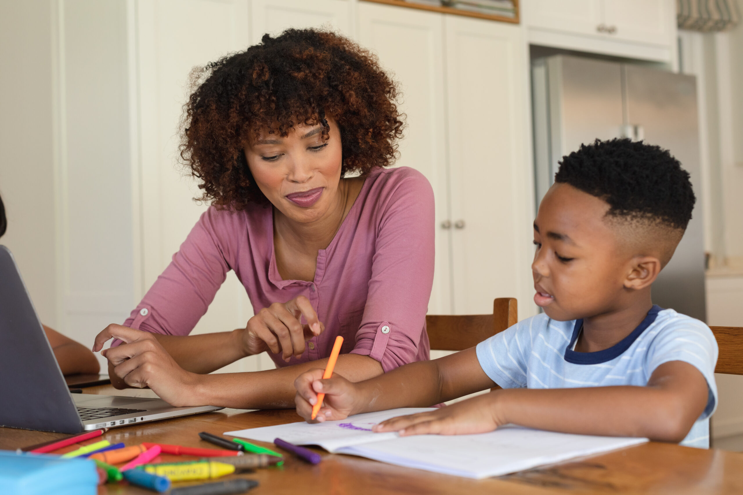 An adult and child working with pencils at a table.
