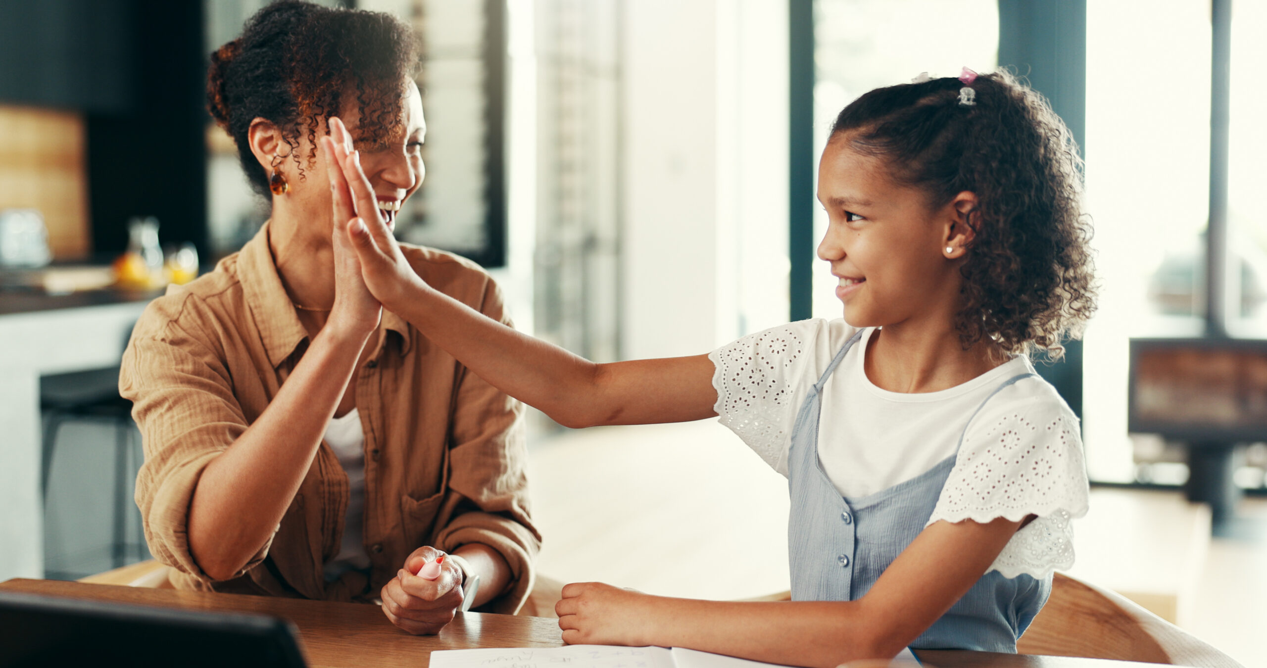 An adult and child sharing a high five at a table.