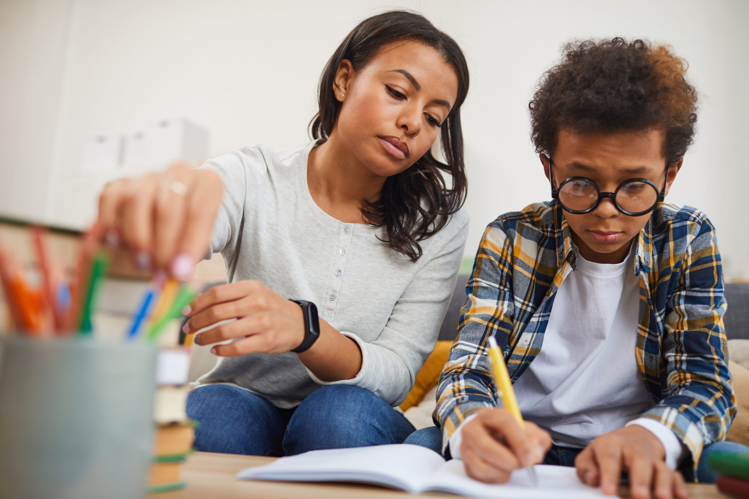An adult supporting a child with writing at a table.